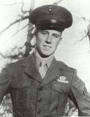 Male US Marine in green jacket and hat with hands on hips and trees in background