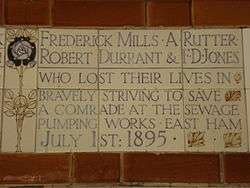 A tablet formed of five tiles of varying sizes, bordered by yellow and blue flowers in an art nouveau style. The tablet reads "Frederick Mills, A Rutter, Robert Durant & F. D. Jones who lost their lives in bravely striving to save a comrade at the sewage pumping works, East Ham July 1st 1895".