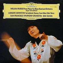 Photo of Seiji Ozawa, wearing a flowered white shirt, and conducting an orchestra
