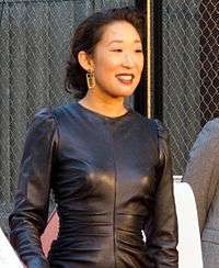 A photo of Sandra Oh, wearing a black dress and smiling towards the public.
