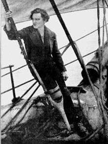 Barrymore, cleanshaven, standing in costume as Captain Ahab, including a false right peg-leg, holding onto ship's rigging