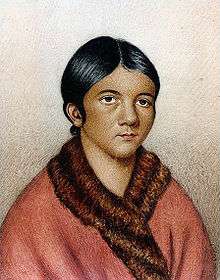 "A bust color portrait of a young Aboriginal woman, in a red traditional shawl with her dark hair tied back "