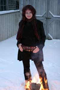 Sheri-D Wilson standing in snow with a fire at her feet.