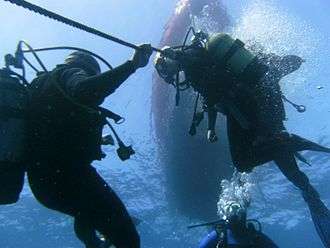 Divers holding onto a rope anchor cable as an aid to depth control during a decompression safety stop