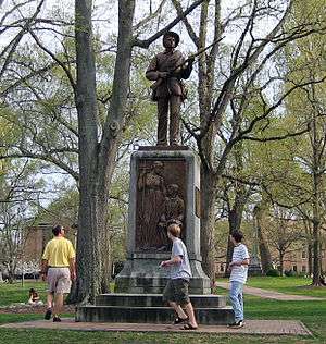 A statue of a soldier with three people walking around the base.