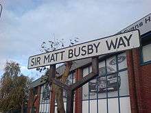 A white road sign with a black border and the words "Sir Matt Busby Way" in black capital letters.