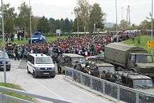 large group of migrants moving along a road, being directed by the army and police