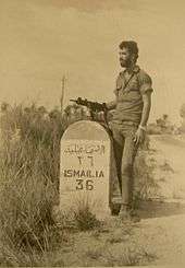  A soldier with an Uzi next to a road sign reading "ISMAILIA 36"