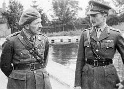 Two men in military uniforms with Sam Browne belts. The one on the left is wearing a beret, while the one on the right has a peaked cap.