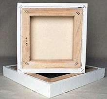 A square canvas rests atop another with its back showing a thick frame of wood.