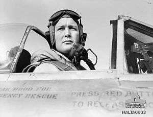 Black and white photo of a man wearing a flying helmet sitting in the cockpit of an aircraft