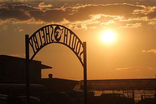 An archway that says South Shelby right outside of their football stadium. There is a beautiful golden sunset in the background.