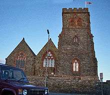 The west end of a red sandstone church with two gables and a battlemented tower