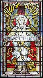 The image on the glass is of an angel in full frontal with wings outstretched behind and above holding a banner that reads "Praise Ye the Lord"
