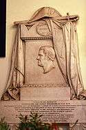 Photograph of a marble memorial carved with the image of James Brisbane in profile, carved cloth over the top and text on a panel beneath