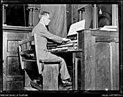 alt=A black and white photo of a man playing the organ showing the keyboard and the pedals