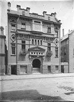 Old photo of the front of the former Hall showing its complex details. It was built of brick with a rusticated basement, balconies with curved wrought iron balustrades, a large entrance stairway under a prominent pediment and Art Nouveau panels.