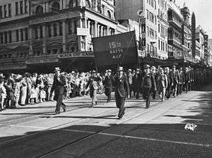 Men in suits and hats march down a city street with a banner