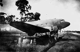Twin-engined transport plane parked on a field near a fence