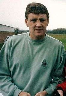 A brown-haired man in a light green sweatshirt with a neutral expression