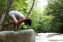 person in crow pose next to a stream