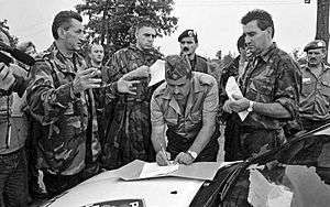 Colonel Bulat signing surrender on a police car bonnet while Lieutenant General Stipetić and Mr. Pajić observe.