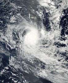 A true-color image showing a tropical cyclone with cloud bands and a central area of clouds. The outlines of some islands hidden under the clouds are also shown.
