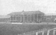 View towards one end of the ground, showing a roof, supported by several pillars and bearing a clock, covering the central part (behind the goal) of an otherwise open terrace