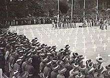 Soldiers in slouch hats stand around a square of white crosses during a ceremony at a war cemetery
