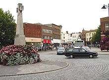 Street scene showing roads and shops around a stone cross.