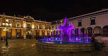 Violet-lit fountain on a city square at night