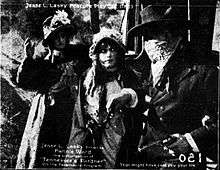 A masked man with a gun looks at two women in front of him
