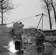 A tank crew brew up with a benghazi burner, at a stop in November 1944 during the Liberation of Holland. The tank behind is a Churchill AVRE, Armoured Vehicle Royal Engineers, carrying a portable Small Box Girder Bridge