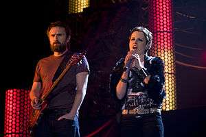 Noel Hogan holding a guitar and Dolores O'Riordan singing into a microphone