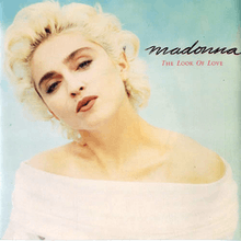 Madonna looks towards the front and tilts her head to the right. She is wearing a white dress, with bare shoulders.