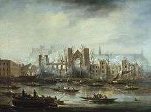 A view of Parliament, burned out, from the South bank of the Thames. The outline of a large gable ended building is visible in the middle of the complex; there is much smoke around the image. Several boats are visible on the river, looking at the building.