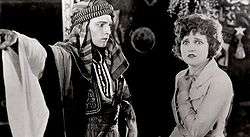 Black and white screenshot from the film The Sheik, with the man in Arab costume and the woman in Western clothing.