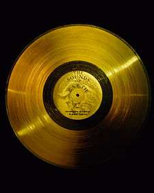 Flat circular disc of gold, with a central label, a hole, and a wide band of very small lines, like a golden version of an old analog record