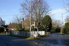 Street scene with area between two roads containing trees and stone column behind a white fence.