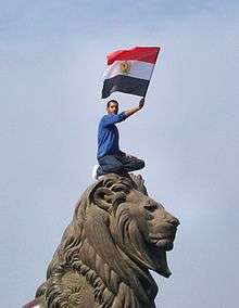 Man crouched on top of the famous Qasr al-Nil Bridge stone lions, waving the Egyptian flag