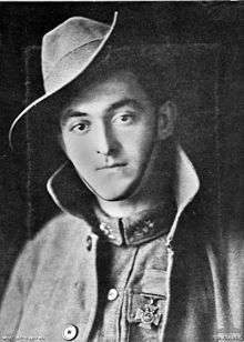 Portrait photograph of soldier wearing a medal shaped like a cross on his left breast. He is wearing a slouch hat and a greatcoat that is unbuttoned
