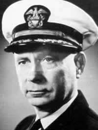 Black-and-white photo of a man in naval uniform from the shoulders up. He wears a terse expression and an United States Navy officers hat.
