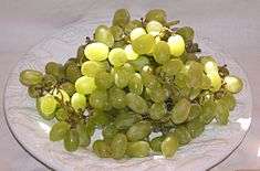 On a white plate rests a cluster of golden, green-colored Thompson Seedless grapes.