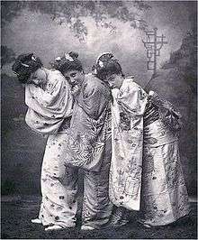 Bond with two women on stage dressed in kimonos, scenery in background.