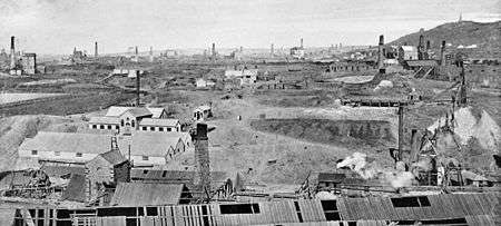 Barren landscape with a large number of tall smoking chimneys and long low buildings