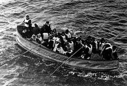 Photograph of a lifeboat, filled with people wearing life jackets, being rowed towards the camera.
