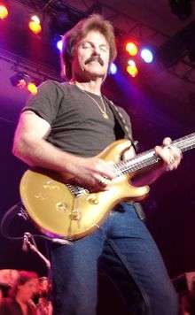 Johnston playing a soulful Paul Reed Smith Artist's Gold Top lead wearing a black t-shirt and jeans, in front of colorful stage lights