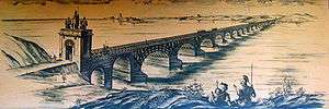 Am artist's interpretation of Trajan's Bridge depicted upon a light brown surface, with bridge stretching from near shore of river on the bottom left and the far shore in the top right.