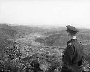 Man in dark-coloured military uniform and peaked cap looking over a valley