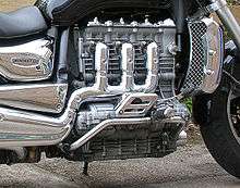 Closeup picture of a motorcycle engine with three heavily chromed exhaust pipes coming out of the side